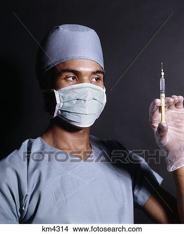 Picture - 1970S African-American Man Doctor Nurse Surgical Mask Gown Gloves Holding Hypodermic Syringe Needle Injection Shot. Fotosearch