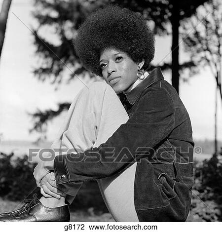 Stock Image - 1970S Afro-American Portrait Woman Seated Bringing Knees To Chest With Cheek Resting On Leg Looking Off Into Distance. Fotosearch