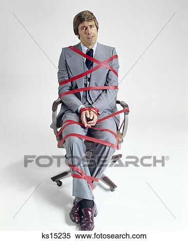 1970S Business Man Tied Up In Red Tape Sitting On Office Desk Chair Symbolic View Large Photo Image Stock Photography - 1970S Business Man Tied Up In Red Tape Sitting On Office Desk Chair Symbolic . Fotosearch