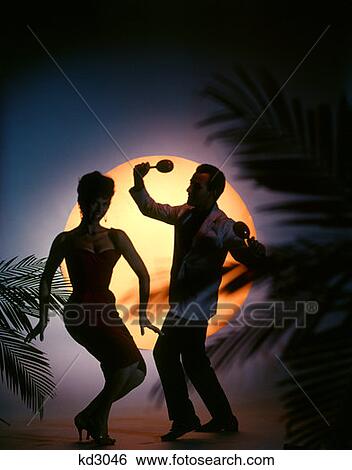 Stock Photograph - 1970S Couple Dancing In Front Of Full Moon On Tropical Beach With Palm Trees Man Woman Maracas Vacation Silhouette . Fotosearch
