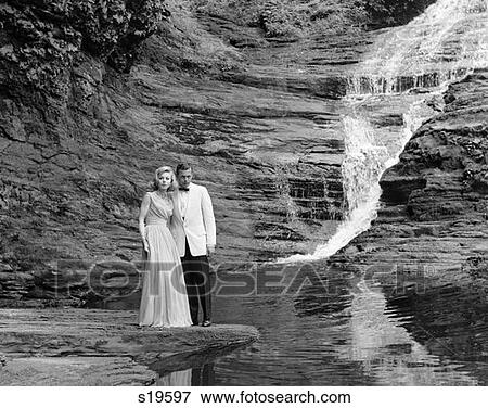 1970S Couple In Formal Dress Standing On Rock At Side Of Creek With Waterfall Coming Down Behind Them View Large Photo Image Stock Photo - 1970S Couple In Formal Dress Standing On Rock At Side Of Creek With Waterfall Coming Down Behind Them . Fotosearch