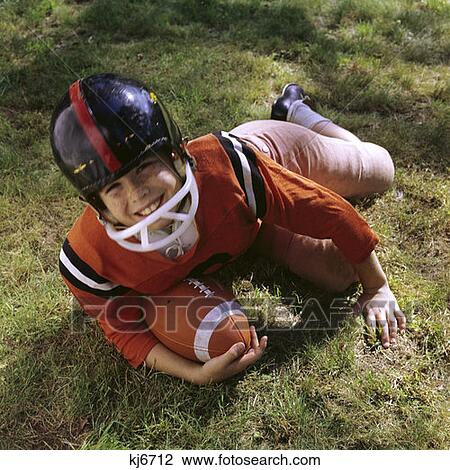 1970S Freckle Faced Boy Football Uniform Helmet Orange Top Pink Pants Lying In Grass Holding Football Look Up At Camera View Large Photo Image Stock Image - 1970S Freckle Faced Boy Football Uniform Helmet Orange Top Pink Pants Lying In Grass Holding Football Look Up At Camera. Fotosearch