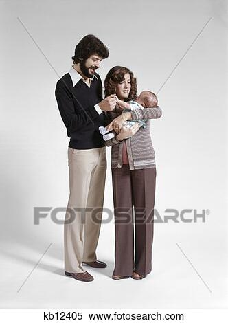Stock Photography - 1970S Full Length Portrait Standing Family 3 Mother Father Baby Man Woman Child. Fotosearch