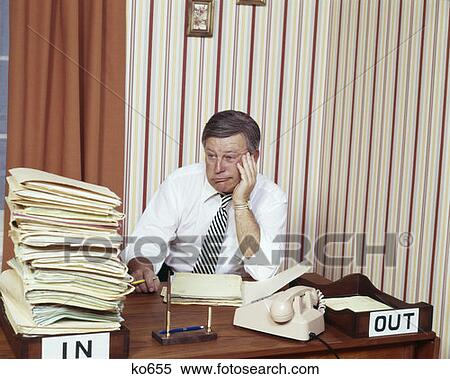 Stock Photography - 1970S Man Desk Funny Facial Espression Overwhelmed Big Pile Papers Folders Work In Box In-Box Work Workload . Fotosearch
