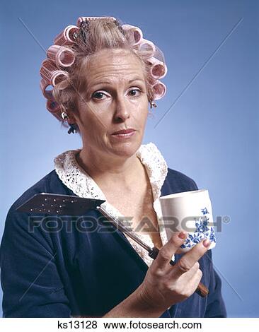 Stock Photo - 1970S Middle Aged Woman Wearing Curlers Robe Holding Egg Turner Spatula Coffee Mug Housewife Morning Breakfast. Fotosearch