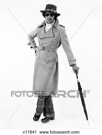 Stock Image - 1970S Portrait Of Black Male Dressed In Raincoat & Hat Leaning On Umbrella . Fotosearch