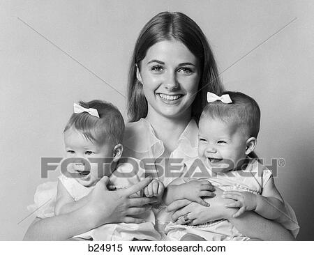 Stock Photography - 1970S Portrait Of Smiling Mother With Arms Around Twin Girls With Bows In Hair . Fotosearch