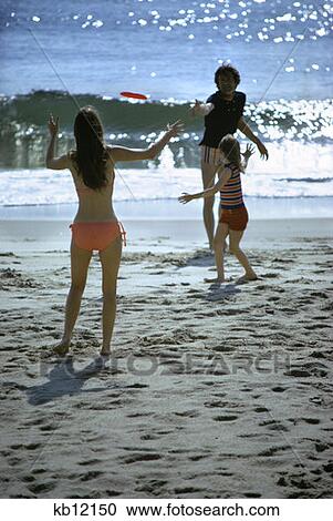1970S Retro Family Man Woman Girl Father Mother Daughter Together Throwing Frizbee On Beach At Seashore View Large Photo Image Stock Image - 1970S Retro Family Man Woman Girl Father Mother Daughter Together Throwing Frizbee On Beach At Seashore. Fotosearch