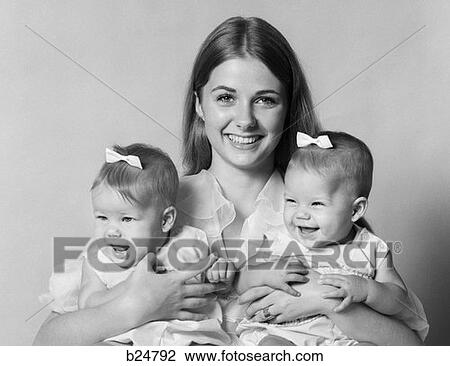 1970S Smiling Mother Holding One Female Twin With Bow In Hair Under Each Arm View Large Photo Image Stock Image - 1970S Smiling Mother Holding One Female Twin With Bow In Hair Under Each Arm . Fotosearch