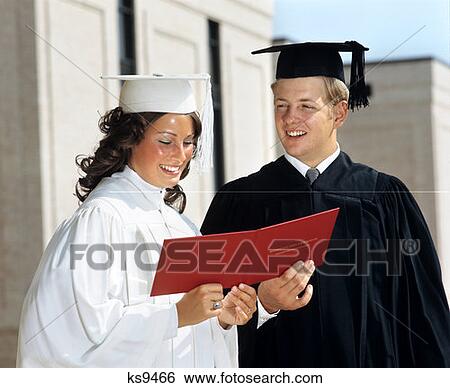 1970S Teen Couple Girl White Robe Boy In Black Robe Mortarboard Hold Red Diploma Between Them High School Smiling Proud View Large Photo Image Stock Photograph - 1970S Teen Couple Girl White Robe Boy In Black Robe Mortarboard Hold Red Diploma Between Them High School Smiling Proud. Fotosearch