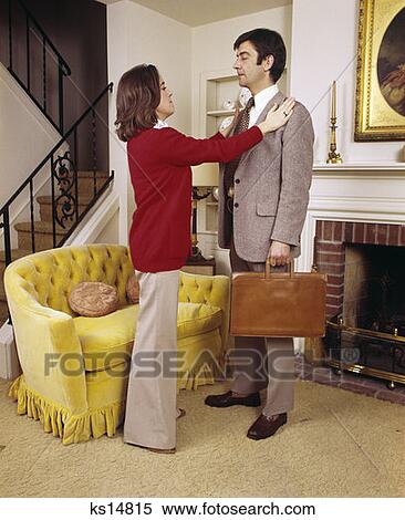 Stock Photography - 1970S Wife Adjusting Jacket Of Executive Husband Ready To Leave For Work Couple Man Woman. Fotosearch