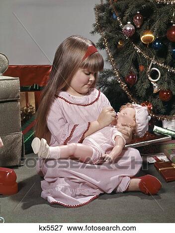 1970S Young Girl Nightgown And Slippers Sitting By Christmas Tree Giving Doll Baby A Bottle View Large Photo Image Stock Photo - 1970S Young Girl Nightgown And Slippers Sitting By Christmas Tree Giving Doll Baby A Bottle. Fotosearch
