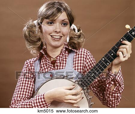 1970S Young Woman In Checked Shirt And Overalls With Hair In Ponytails Playing Banjo Strum Rube Bumpkin Country View Large Photo Image Stock Photography - 1970S Young Woman In Checked Shirt And Overalls With Hair In Ponytails Playing Banjo Strum Rube Bumpkin Country. Fotosearch