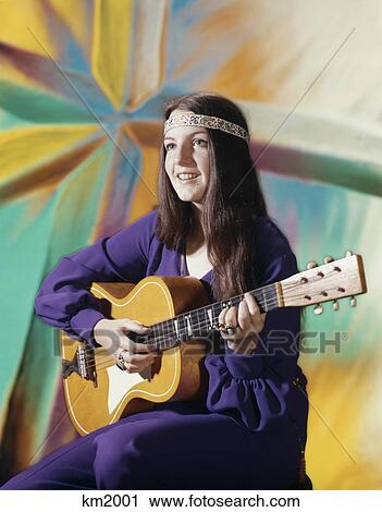 1970S Young Woman Wearing Purple Dress And Beaded Headband Playing Acoustic Guitar Patterned Background Folk Song View Large Photo Image Stock Image - 1970S Young Woman Wearing Purple Dress And Beaded Headband Playing Acoustic Guitar Patterned Background Folk Song. Fotosearch