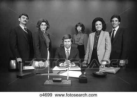 1980S Group Portrait Of Office Staff Standing Behind Desk Around Boss With Serious Expressions View Large Photo Image Stock Photo - 1980S Group Portrait Of Office Staff Standing Behind Desk Around Boss With Serious Expressions. Fotosearch