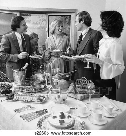 Stock Photography - 1980S Pair Of Couples Chatting Over Food & Drinks At Buffet Table . Fotosearch