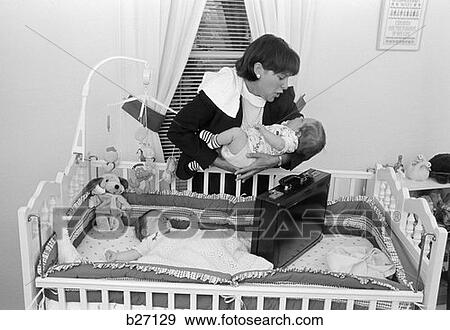 1980S Working Mother Standing Over Crib Holding One Baby While Other Sleeps Briefcase In Crib Indoor View Large Photo Image Stock Photo - 1980S Working Mother Standing Over Crib Holding One Baby While Other Sleeps Briefcase In Crib Indoor . Fotosearch