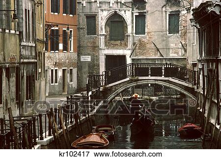 Stock Photo - Canal Between Buildings Gondolier Rowing Gondola Under Bridge Venice Italy . Fotosearch