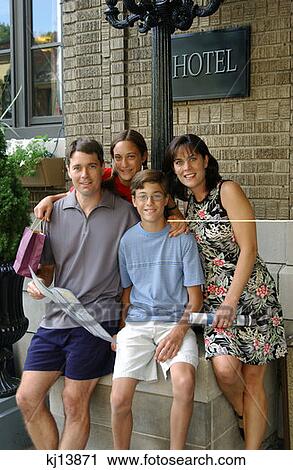 Stock Image - Family Of Four Posing Outside Hotel, Tourists. Fotosearch