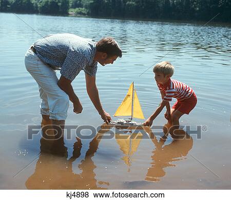 Father And Son Pushing A Toy Sailboat In A Lake Retro 1970 1970S View Large Photo Image Stock Photo - Father And Son Pushing A Toy Sailboat In A Lake Retro 1970 1970S. Fotosearch