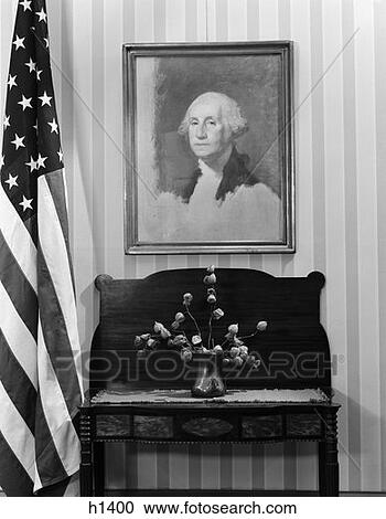 Stock Image - Framed Portrait George Washington Hanging Above Table With Flower Arrangement Next To American Flag . Fotosearch