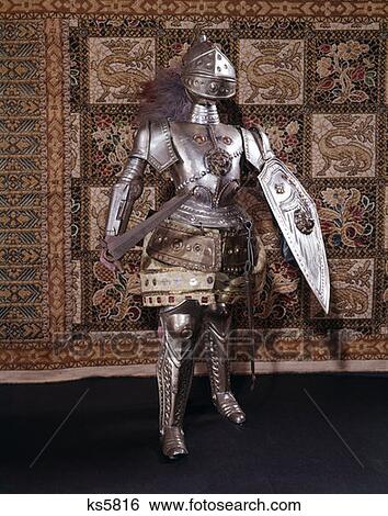 Stock Photograph - Full Length Suit Of Armor Medieval Sword Helmet Shield Metal Knight Chivalry Battle Dress Warrior Tapestry Heraldic. Fotosearch