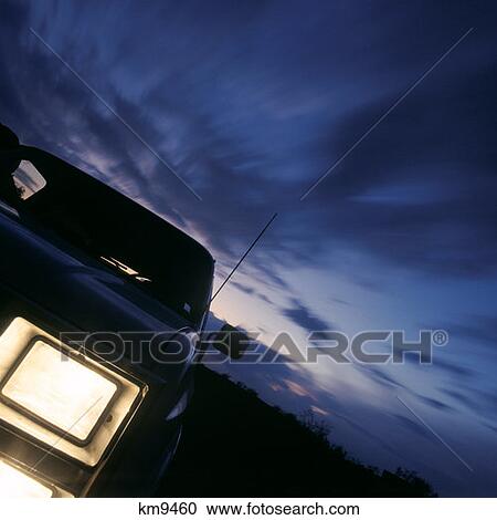 Stock Image - Modern Automobile Headlight And Dark Evening Cloudy Night Sunset Sky. Fotosearch