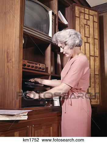 Stock Image - Retro Woman 1970 1970S Playing Records Putting Record On Player. Fotosearch