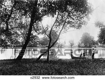 Stock Image - Turn Of The Century Group Of Three Children In Rowboat On Small Lake With Father Standing Next To Them On Land . Fotosearch