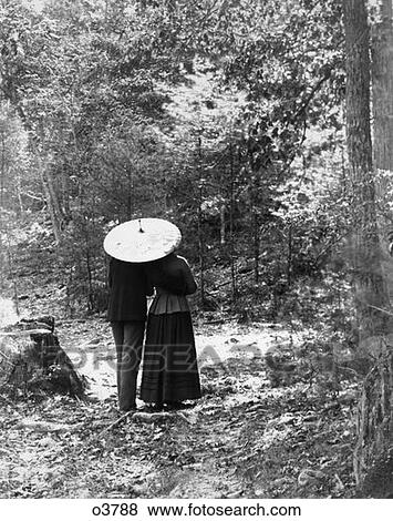 Stock Photo - Turn Of The Century Rear View Of Couple Walking Through Woods Under Umbrella Man With Arm Around Woman . Fotosearch