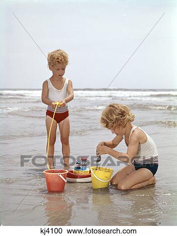 Stock Image - Two Girls Playing In Sand At Beach. Fotosearch