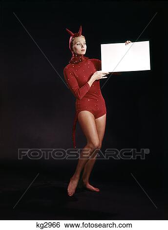 Stock Photograph - Young Woman In Devil Costume Wearing Red Leotard Holding Sign Board In Hands Studio . Fotosearch