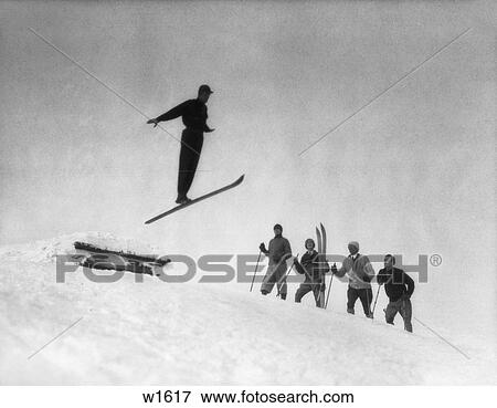 Stock Photo - 1920 1920S Men In Snow Wearing Skis Watching Ski Jumper. Fotosearch