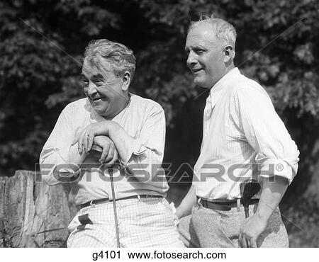 1920S 1930S 2 Elderly Men Holding Golf Clubs Sitting On A Tree Stump Looking Towards Golf Course View Large Photo Image Stock Image - 1920S 1930S 2 Elderly Men Holding Golf Clubs Sitting On A Tree Stump Looking Towards Golf Course . Fotosearch