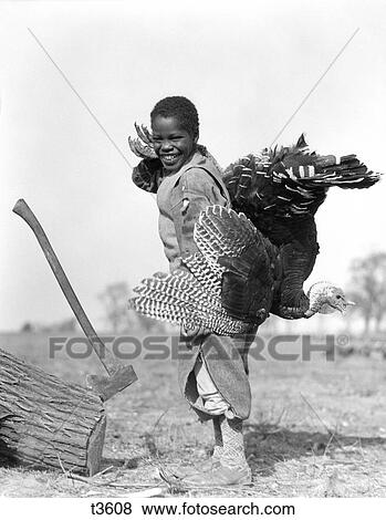 1920S 1930S African-American Boy In Knickers Holding A Live Turkey Over His Shoulder Standing By A Log Embedded With An Ax View Large Photo Image Stock Photo - 1920S 1930S African-American Boy In Knickers Holding A Live Turkey Over His Shoulder Standing By A Log Embedded With An Ax. Fotosearch
