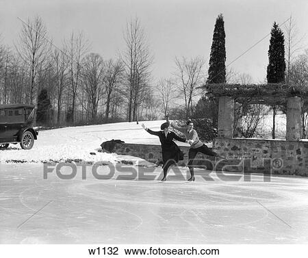 Stock Image - 1920S 1930S Couple Man Woman Ice Skating On Outdoor Rink With Car Nearby Skating Side By Side . Fotosearch