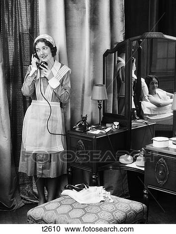 1920S 1930S Maid In Uniform Talks On Telephone In Front Of Vanity Dressing Table Other Woman Is Seen As Reflection In Mirror View Large Photo Image Stock Image - 1920S 1930S Maid In Uniform Talks On Telephone In Front Of Vanity Dressing Table Other Woman Is Seen As Reflection In Mirror. Fotosearch