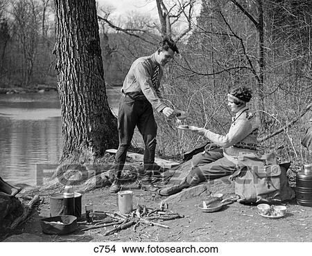 1920S 1930S Man & Woman Camping By Lake Having Picnic Woman Sitting Man Standing Serving Food To Woman East Creek Swamp View Large Photo Image Picture - 1920S 1930S Man & Woman Camping By Lake Having Picnic Woman Sitting Man Standing Serving Food To Woman East Creek Swamp. Fotosearch
