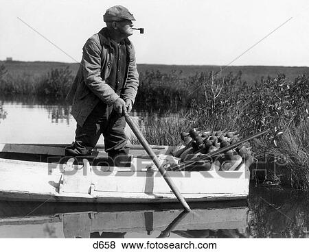 1920S 1930S Senior Man Standing In Boat About To Deploy Duck Decoys In Wetlands Marsh View Large Photo Image Stock Photo - 1920S 1930S Senior Man Standing In Boat About To Deploy Duck Decoys In Wetlands Marsh . Fotosearch