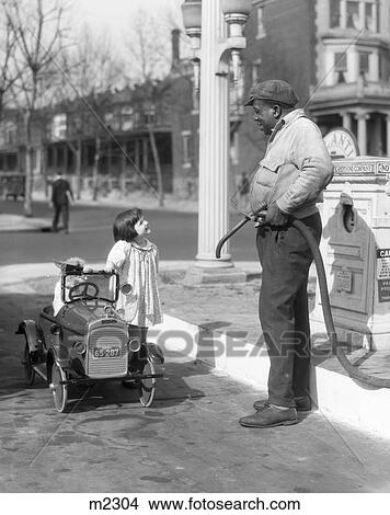 1920S 1930S Smiling Girl Standing Beside Her Pedal Car Asking For Gasoline From Gas Pump Attendant View Large Photo Image Picture - 1920S 1930S Smiling Girl Standing Beside Her Pedal Car Asking For Gasoline From Gas Pump Attendant. Fotosearch