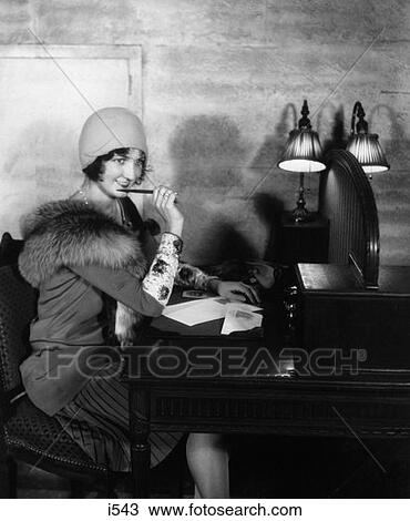 1920S 1930S Smiling Woman With Pen To Lips Writing A Letter At Desk With Lamp In Hotel Lobby Wearing Hat Dress Fur Collar Stole View Large Photo Image Stock Image - 1920S 1930S Smiling Woman With Pen To Lips Writing A Letter At Desk With Lamp In Hotel Lobby Wearing Hat Dress Fur Collar Stole. Fotosearch