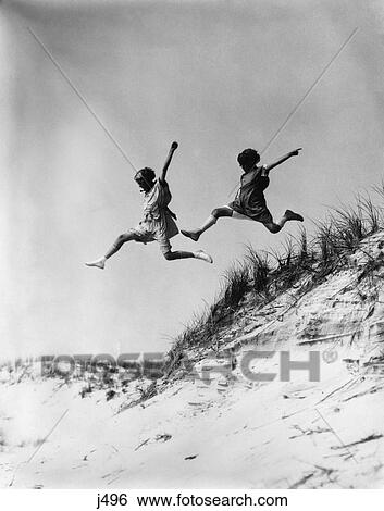 1920S 1930S Two Girls Midair Jumping Off Of Beach Sand Dune  View Large Photo Image Stock Photograph - 1920S 1930S Two Girls Midair Jumping Off Of Beach Sand Dune . Fotosearch