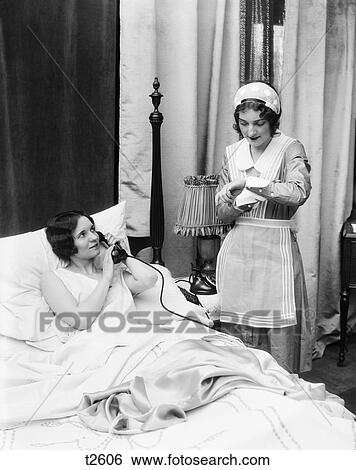 1920S 1930S Two Women In Bedroom Maid Looking At Wrist Watch Other Woman In Bed Talking On Phone Hand Held Over Mouthpiece View Large Photo Image Stock Photograph - 1920S 1930S Two Women In Bedroom Maid Looking At Wrist Watch Other Woman In Bed Talking On Phone Hand Held Over Mouthpiece. Fotosearch