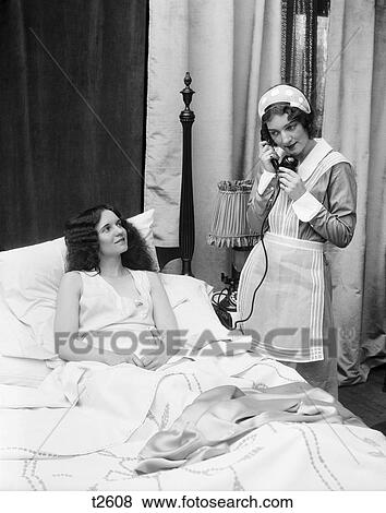 1920S 1930S Two Women In Bedroom One Dressed As Maid On Telephone Other In Bed Smiling Up At Maid Window Curtains Uniform View Large Photo Image Stock Photo - 1920S 1930S Two Women In Bedroom One Dressed As Maid On Telephone Other In Bed Smiling Up At Maid Window Curtains Uniform. Fotosearch