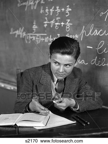 Stock Image - 1920S Boy In Classroom In Front Of Blackboard Aiming Slingshot . Fotosearch