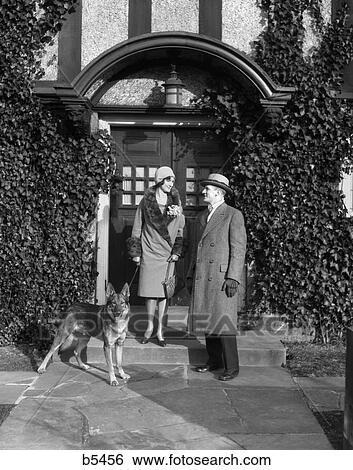 1920S Couple Wearing Coat Hat Gloves On Steps Ivy Covered Building With German Shepherd Dog On A Leash View Large Photo Image Stock Photograph - 1920S Couple Wearing Coat Hat Gloves On Steps Ivy Covered Building With German Shepherd Dog On A Leash. Fotosearch