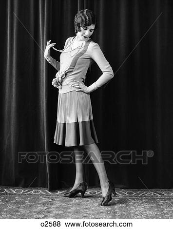 1920S Flapper Woman With Hand On Hip Holding Out String Of Pearls Around Neck Stretching Leg Out & Looking Down & Back At Shoe View Large Photo Image Stock Photo - 1920S Flapper Woman With Hand On Hip Holding Out String Of Pearls Around Neck Stretching Leg Out & Looking Down & Back At Shoe. Fotosearch