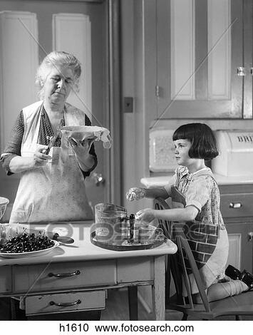 Stock Image - 1920S Grandmother And Granddaughter In Kitchen Preparing A Crust For A Cherry Pie . Fotosearch