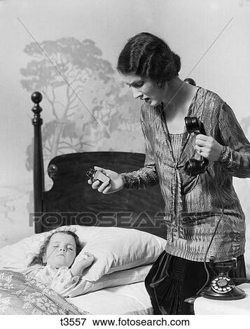 1920S Mother Standing Over Sick Daughter In Bed Holding Telephone In One Hand Medicine Bottle In Other Worried Expression View Large Photo Image Stock Photo - 1920S Mother Standing Over Sick Daughter In Bed Holding Telephone In One Hand Medicine Bottle In Other Worried Expression. Fotosearch