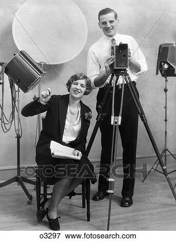 1920S Photographer Standing Behind Camera In Studio With Assistant Sitting Next To Him Holding Paperwork View Large Photo Image Stock Photo - 1920S Photographer Standing Behind Camera In Studio With Assistant Sitting Next To Him Holding Paperwork . Fotosearch